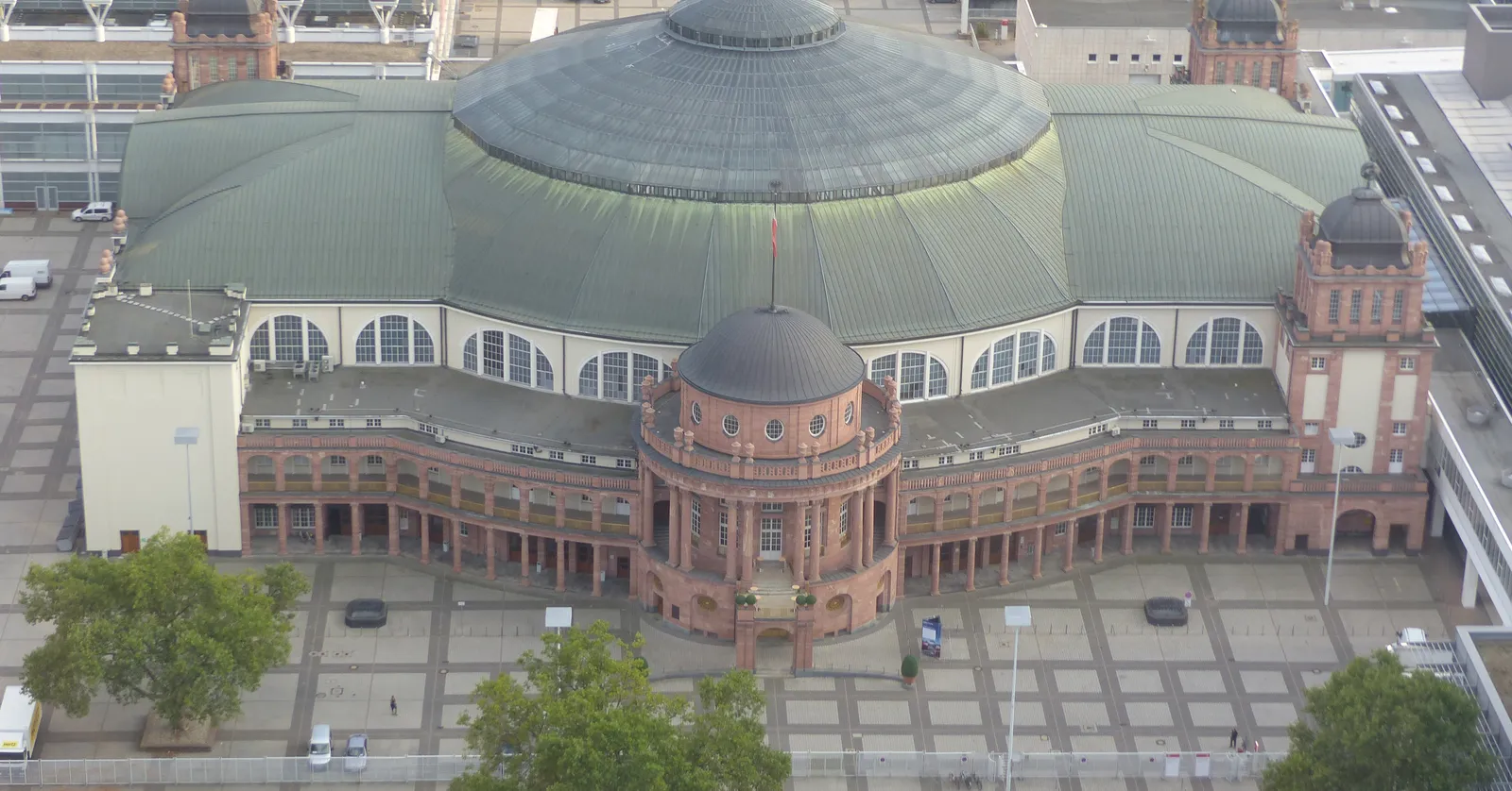 An aerial view of the Festhalle's vast domed roof at the Frankfurt exhibition grounds, with a colonnaded red sandstone base and a paved plaza in front
