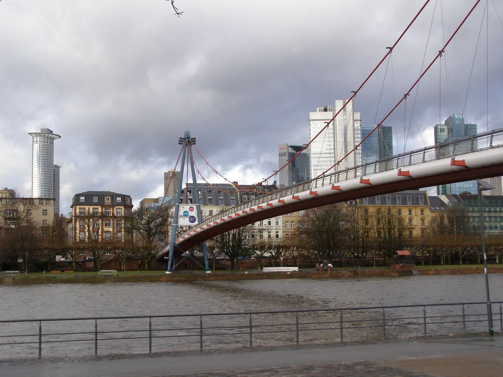 The Holbeinsteg suspension footbridge over the river Main in Frankfurt, its red pylon and cables silhouetted against the city's bank towers