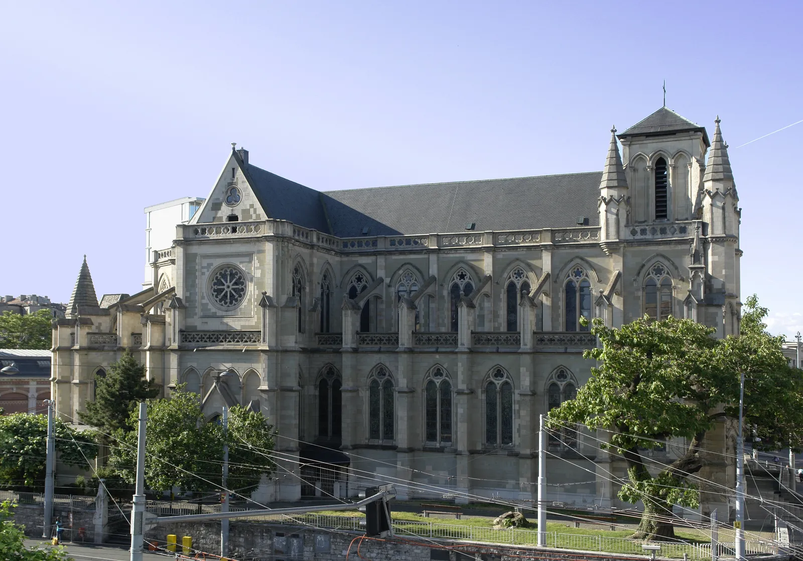The Basilique Notre-Dame in Geneva seen from the side, a grey neo-Gothic church with a rose window, pointed arches and a short tower at the far end
