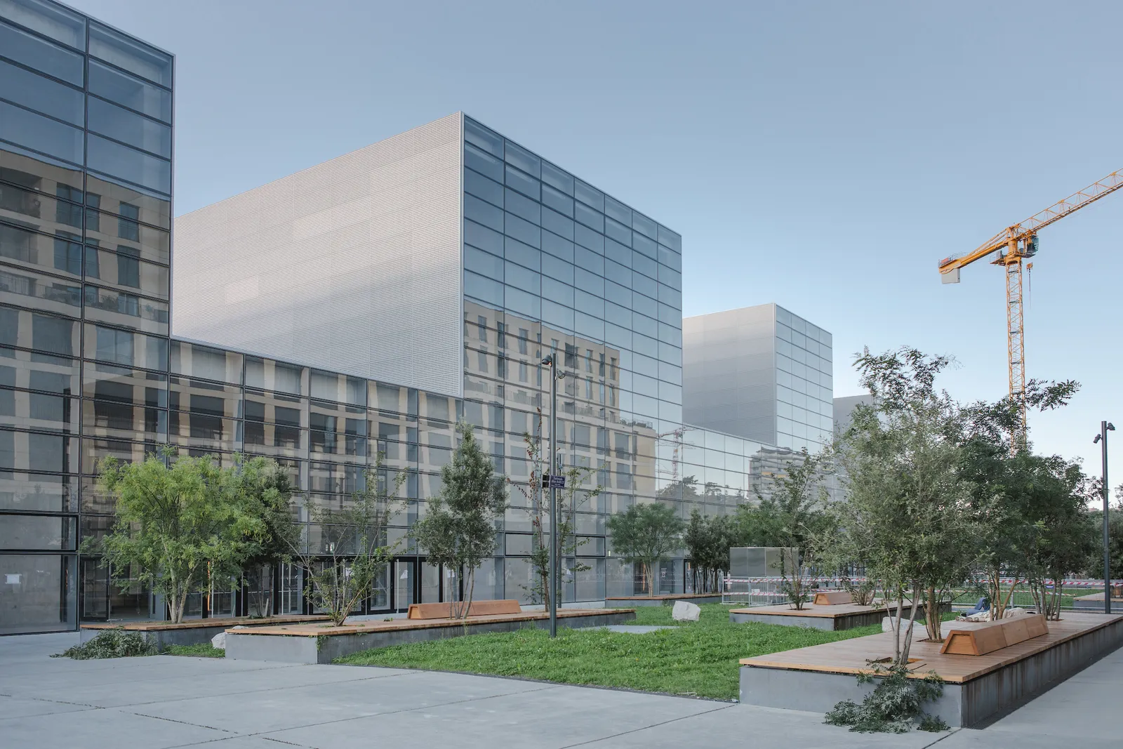 The new district above Eaux-Vives station in Geneva, glass and metal blocks around a paved square with young trees and long timber benches