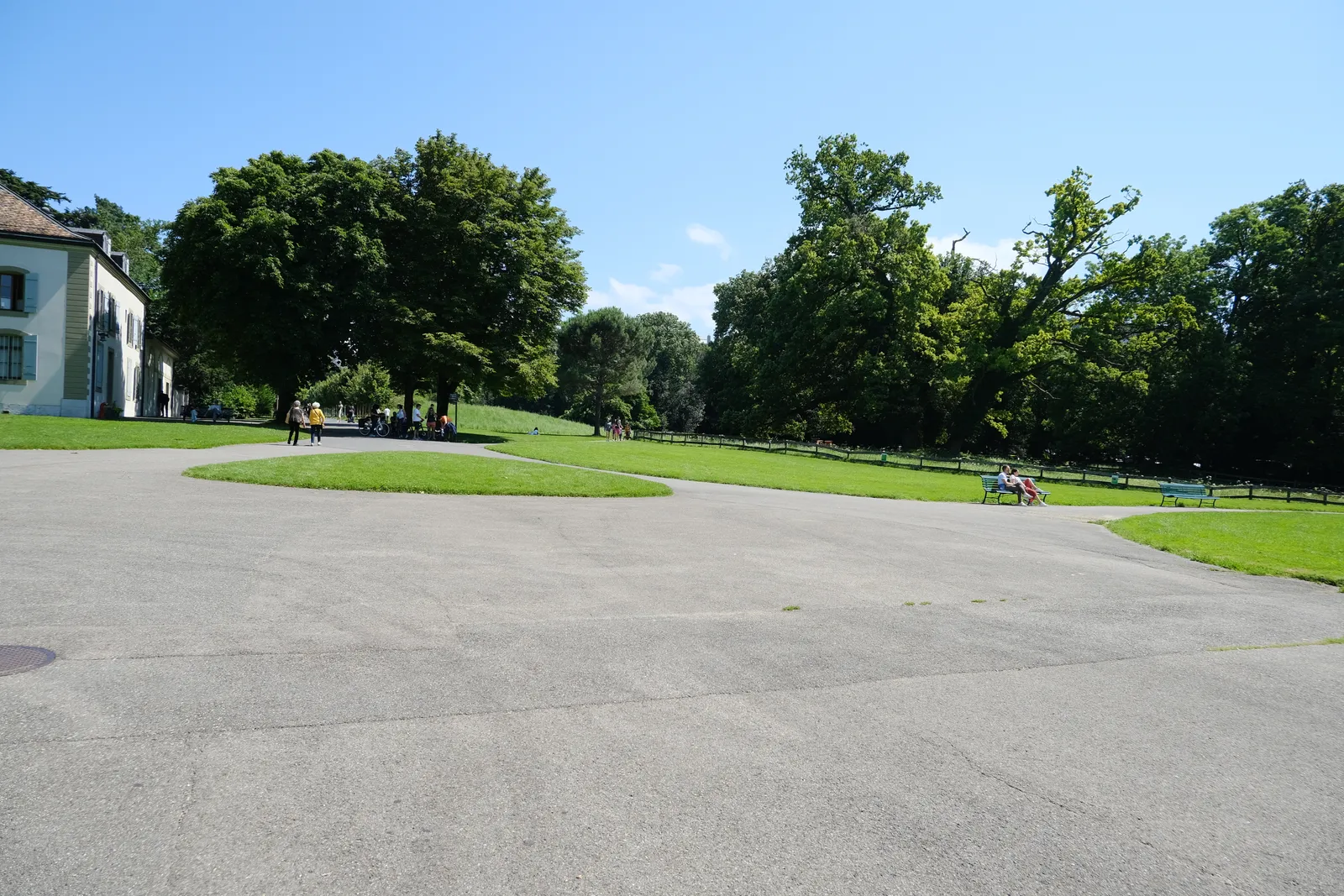 Open lawn and mature trees in Parc La Grange in Geneva, a broad gravel walk curving across the foreground and the corner of the old villa at the left