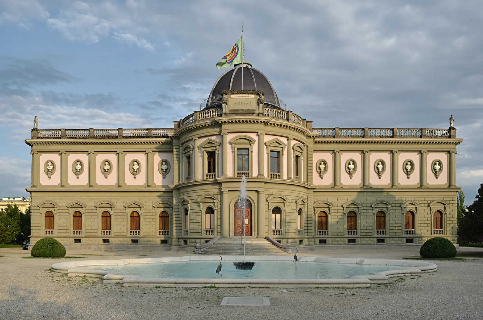 The Musée Ariana in Geneva, a symmetrical 19th-century palace with a domed centre and colonnaded front, a fountain and pool laid out on the lawn before it