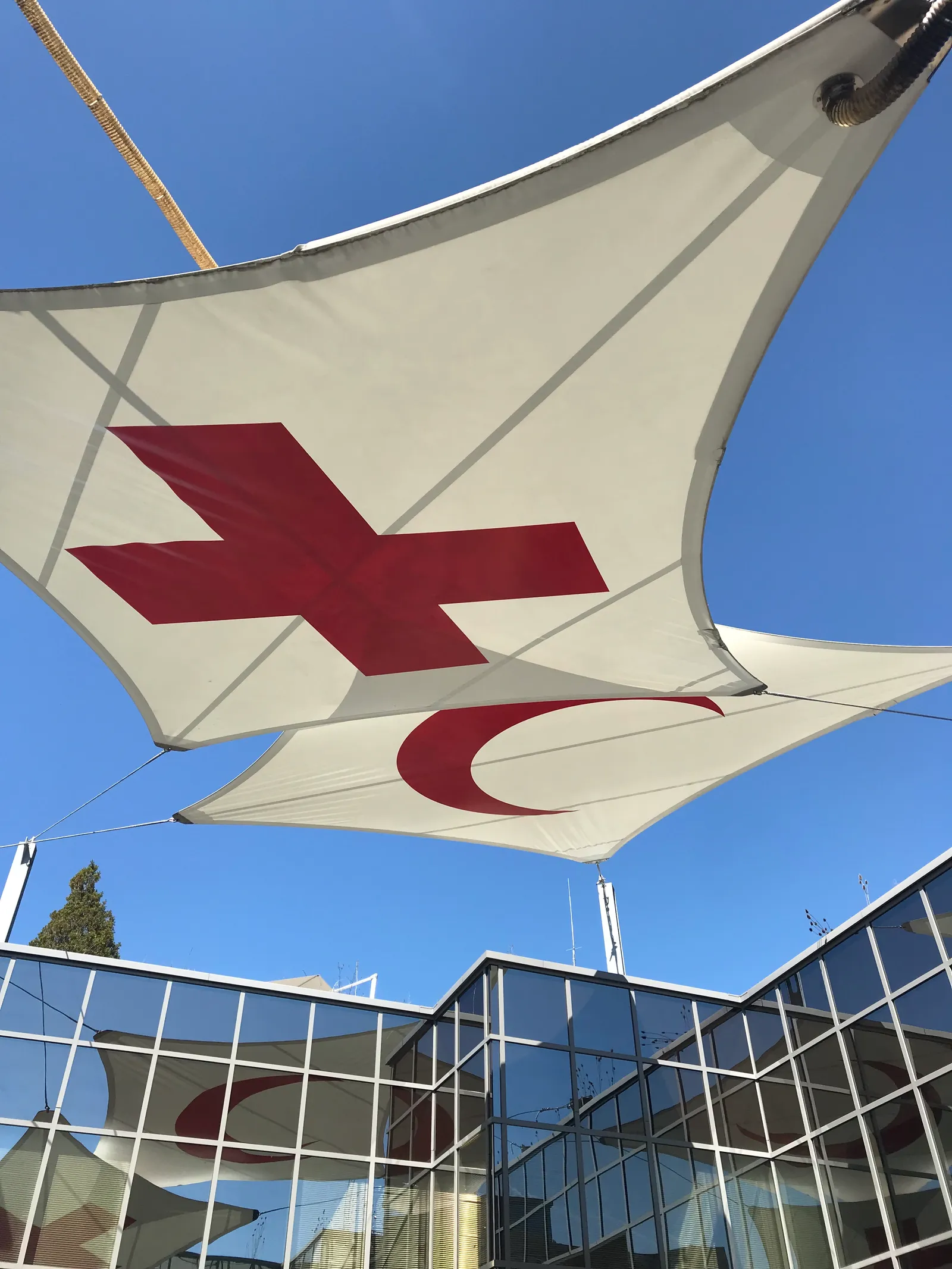 A white fabric canopy printed with a red cross and a red crescent stretched above the glass frontage of the Red Cross and Red Crescent Museum in Geneva