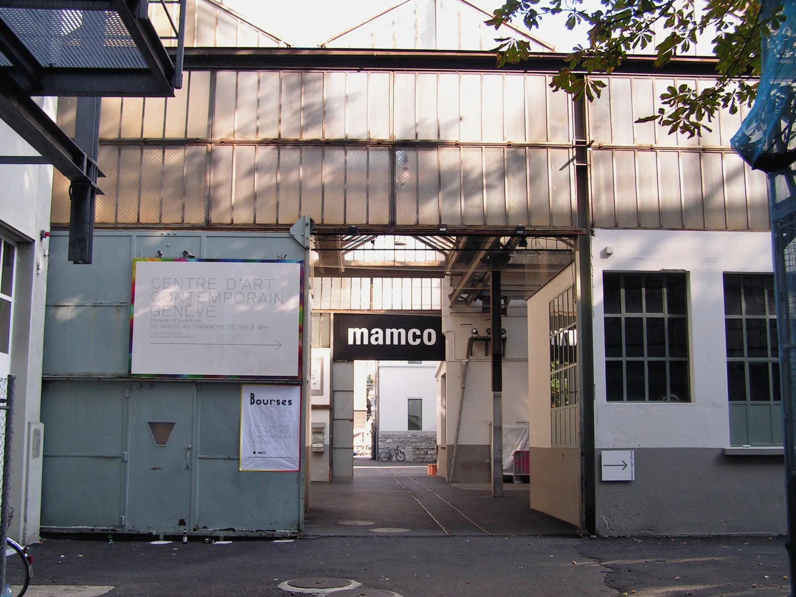 The entrance to MAMCO in Geneva, a gateway through a former industrial building with the museum's name in white lettering above the yard