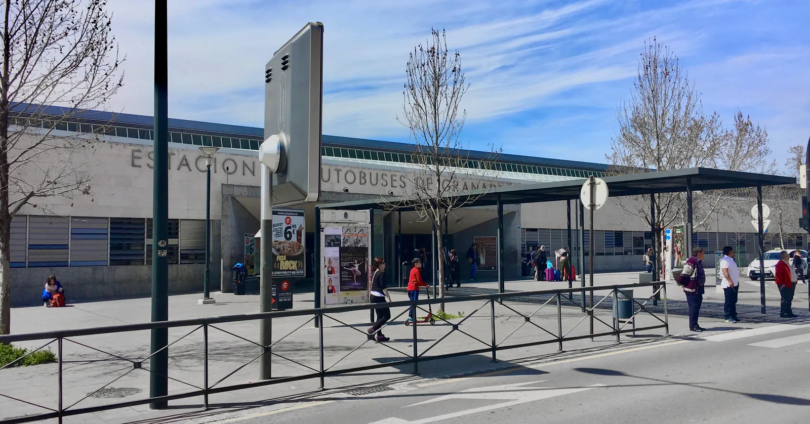 The long, low front of Granada bus station with its name in large letters along the facade, bare trees and passengers crossing the forecourt