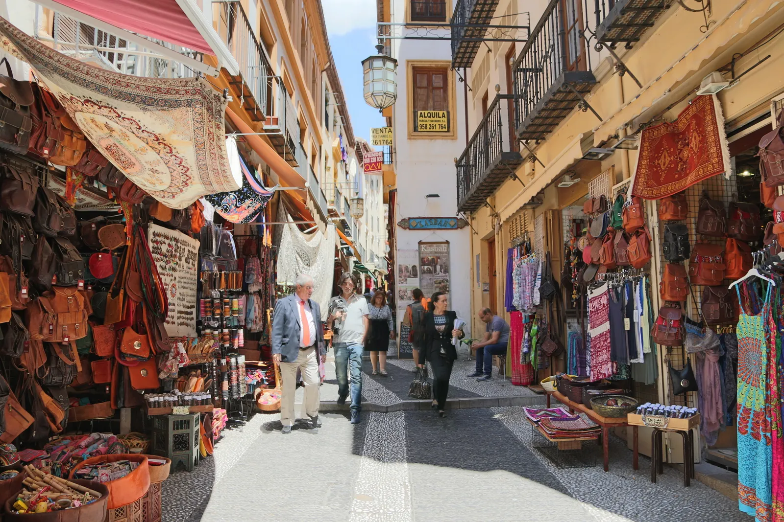 Calle Calderería Nueva in Granada's Albaicín, a narrow sloping lane hung with leather bags, lamps and patterned textiles outside small shops, people walking up between them