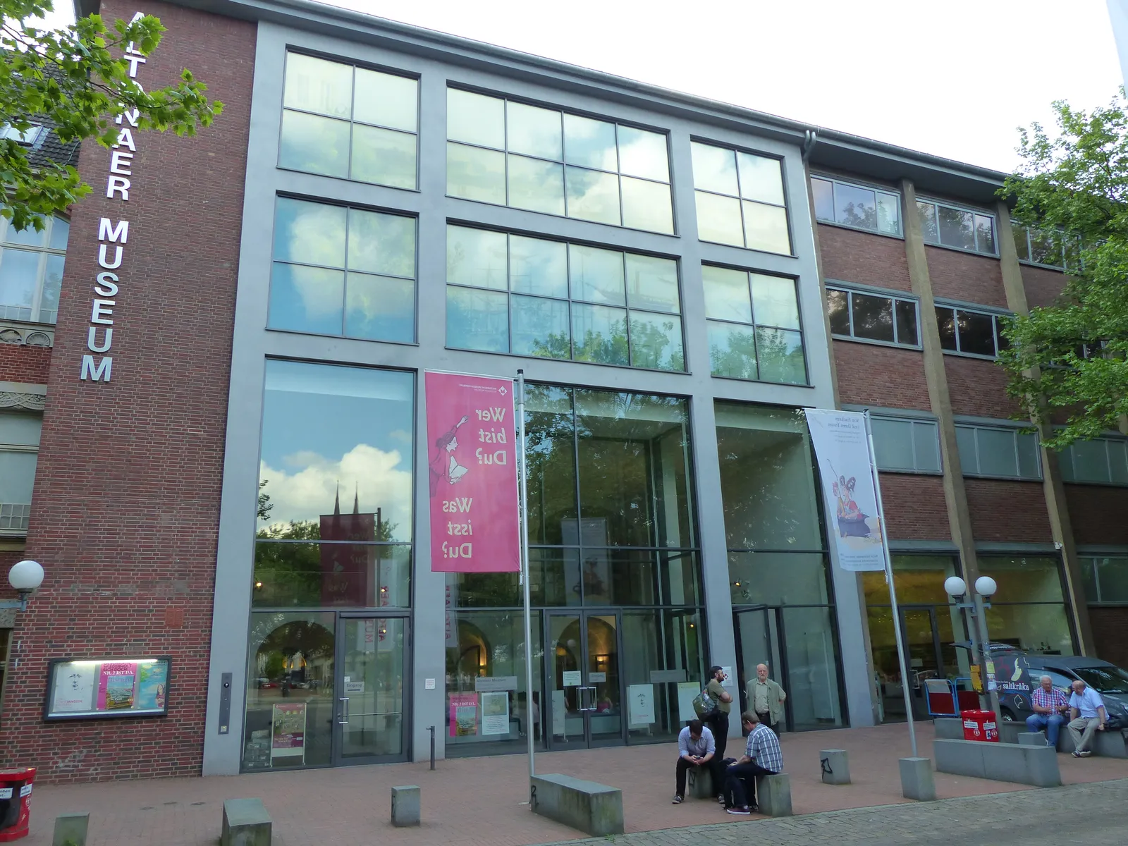 The glass-fronted entrance of the Altonaer Museum in Hamburg, with the museum's name running vertically down the brickwork beside the doors