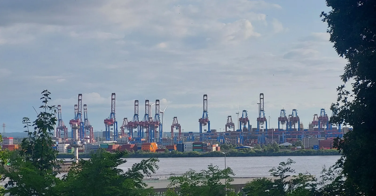 The view from the Altonaer Balkon in Hamburg across the Elbe to a line of red and blue container gantry cranes at the port terminal opposite
