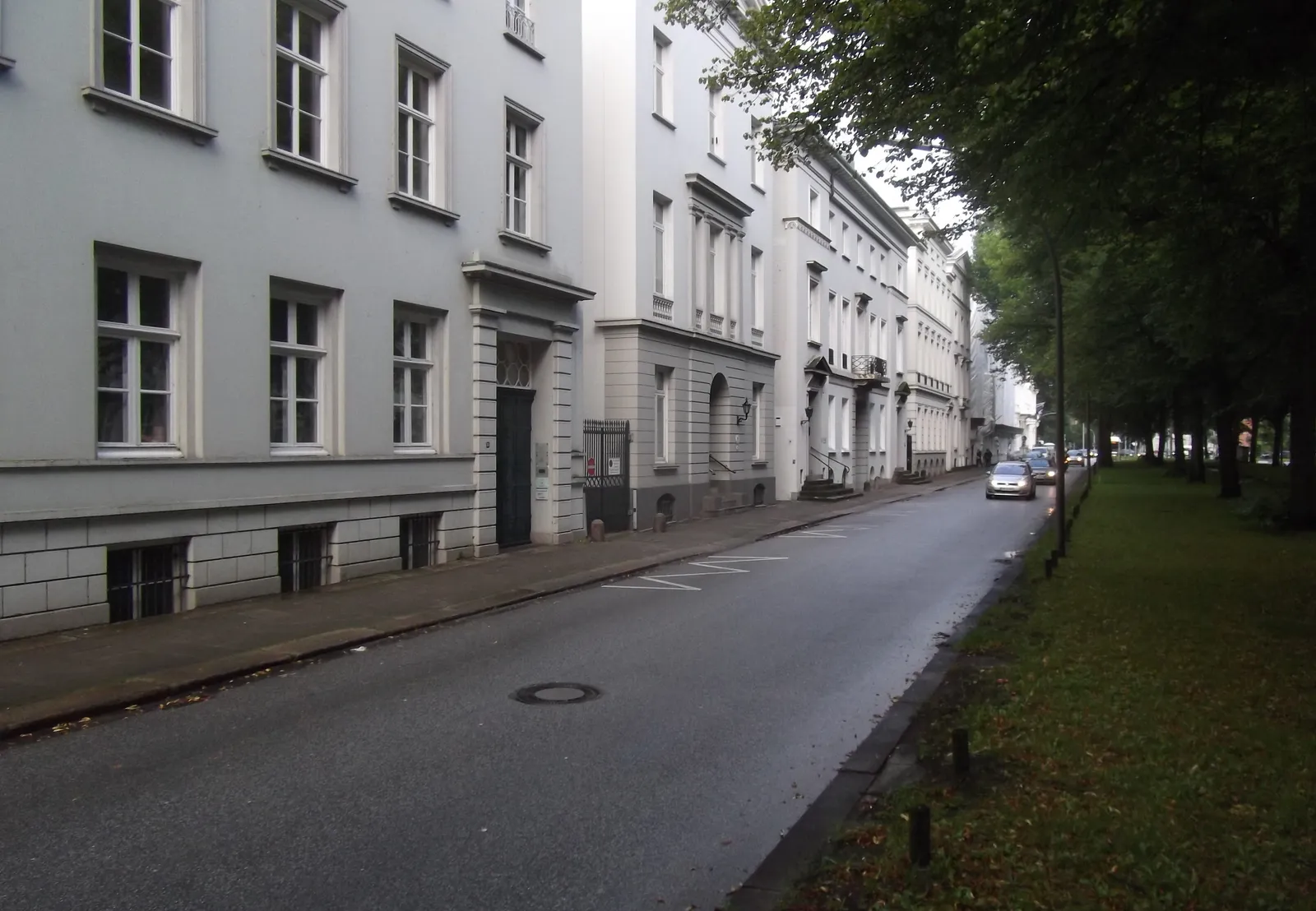 A row of white neoclassical townhouses with columned doorways along Palmaille in Hamburg-Altona, with a tree-lined strip running down the far side of the street