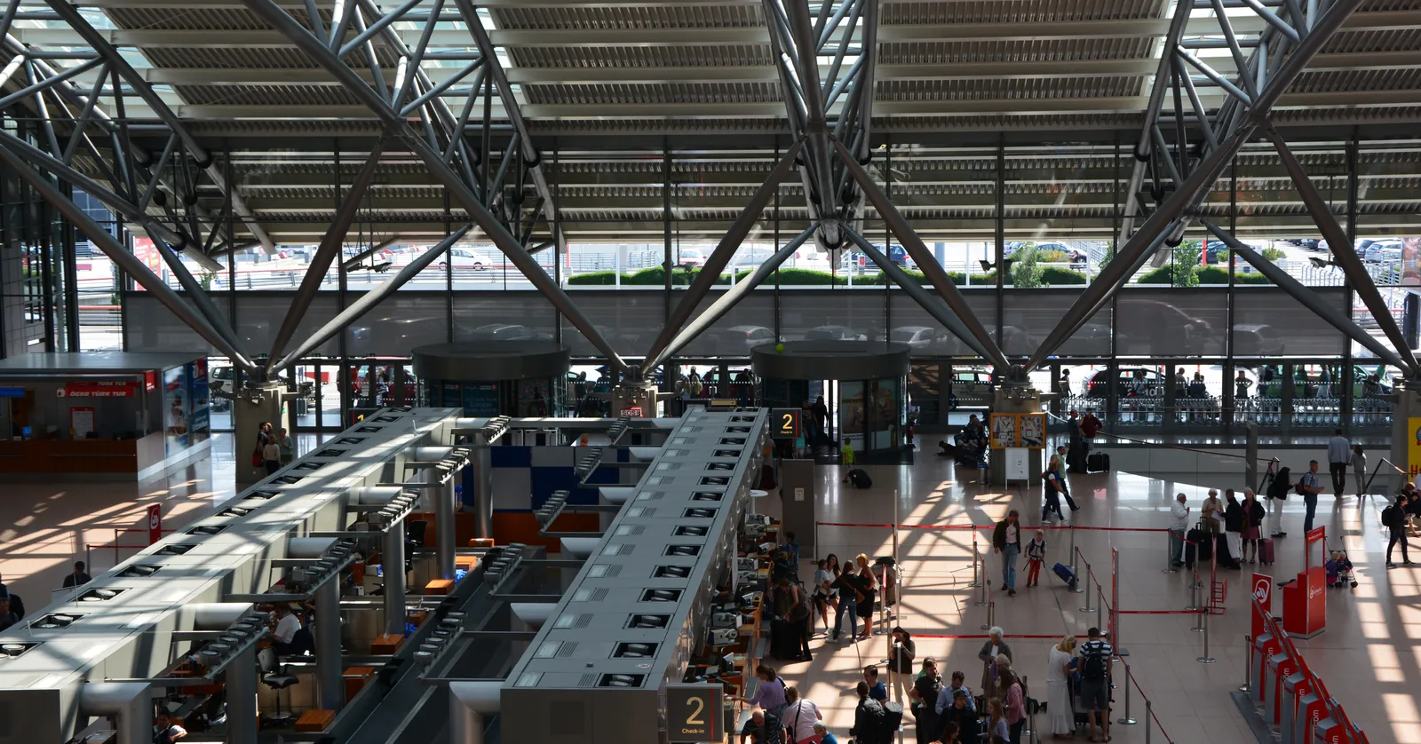 The check-in hall of Terminal 1 at Hamburg Airport seen from a balcony, with a long row of desks under a ribbed steel-and-glass roof and passengers queueing below