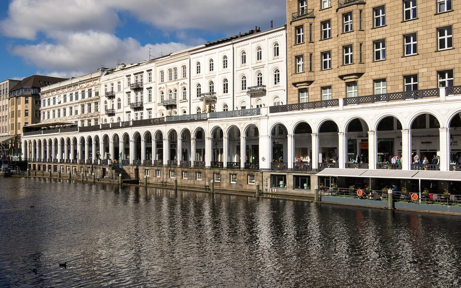 The white arcade of the Alsterarkaden running along the water of the Kleine Alster in Hamburg, with cafe awnings under the arches