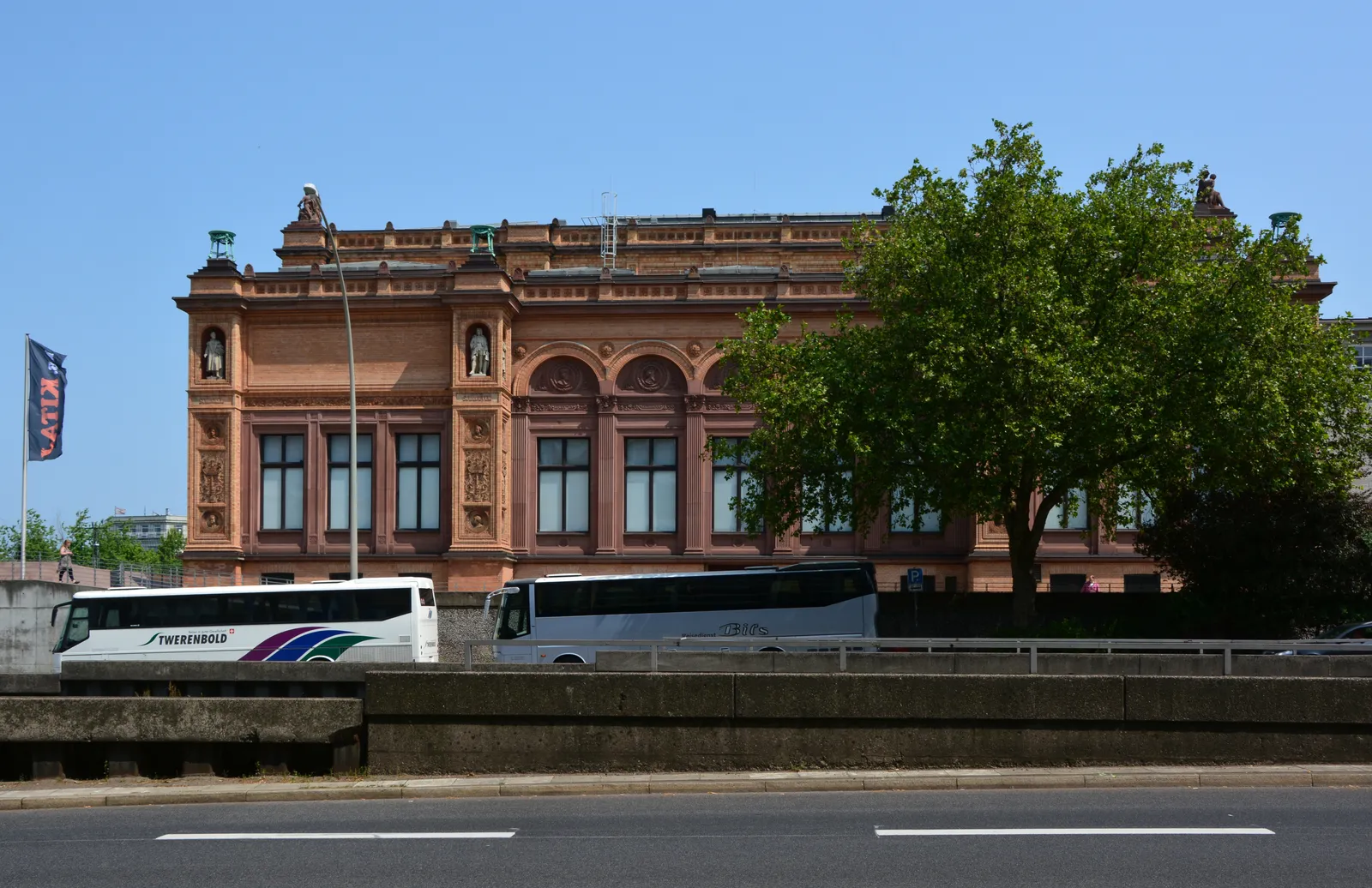 The red-brick main building of the Hamburger Kunsthalle behind a line of trees, seen from the road that runs past the station