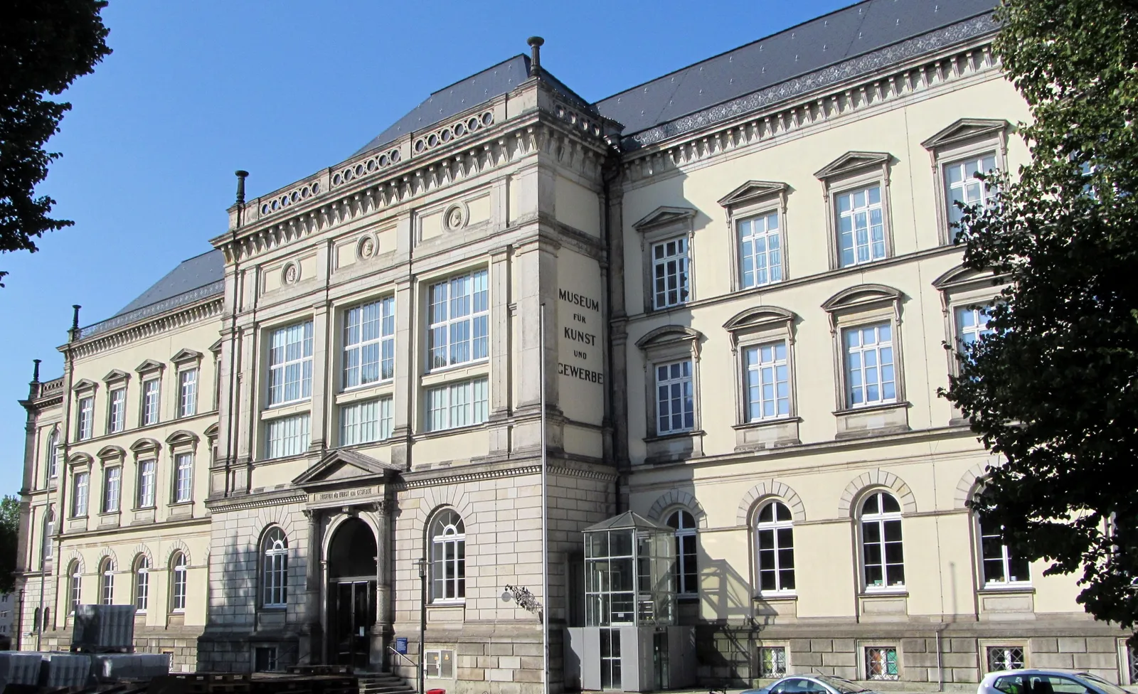 The pale sandstone facade and columned entrance of the Museum für Kunst und Gewerbe on Steintorplatz in Hamburg, with the museum's name carved beside the doorway