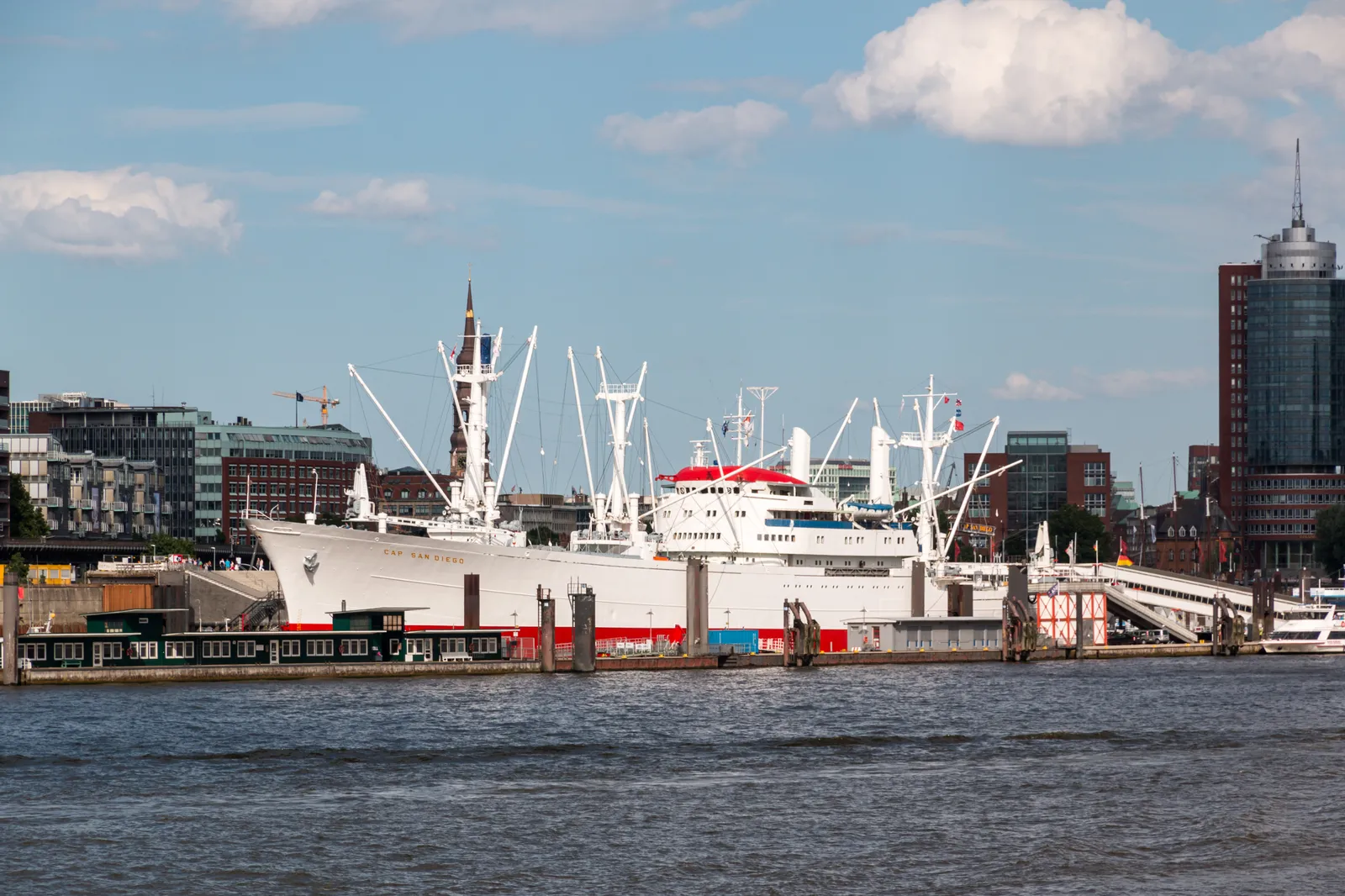 The white cargo liner Cap San Diego moored along a quay in Hamburg, seen across the Elbe with HafenCity buildings behind it