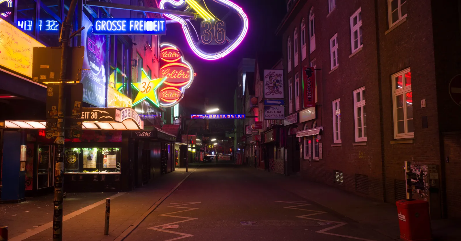 The Große Freiheit side street in Hamburg at night, lit by a large neon guitar sign and rows of coloured club frontages down an otherwise empty road
