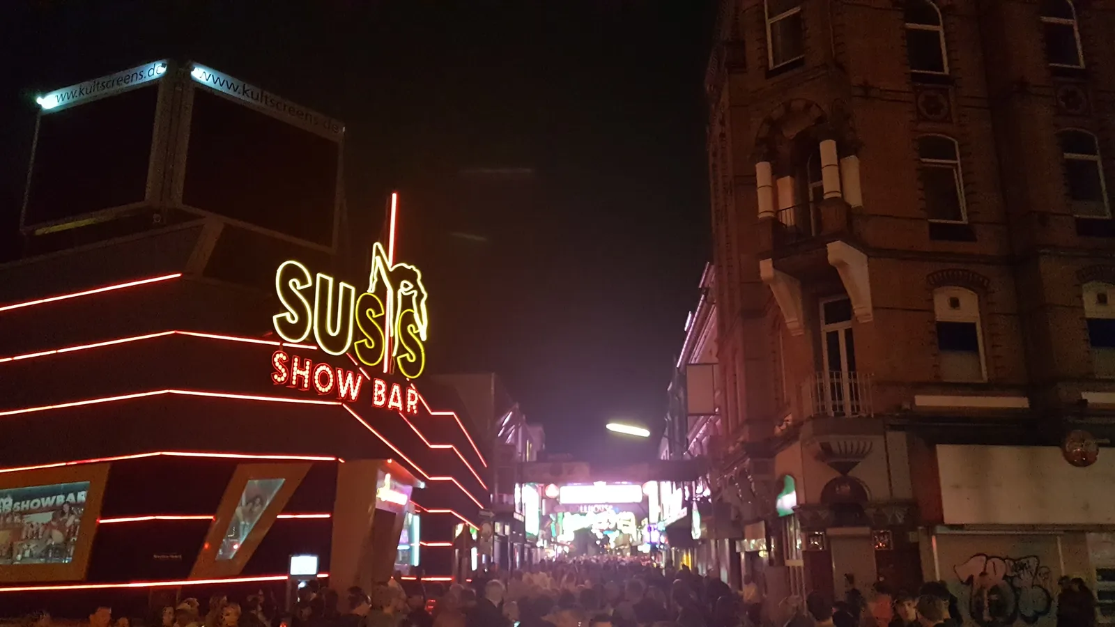 The Reeperbahn in Hamburg after dark, crowded pavements under red and yellow neon signs running down both sides of the street