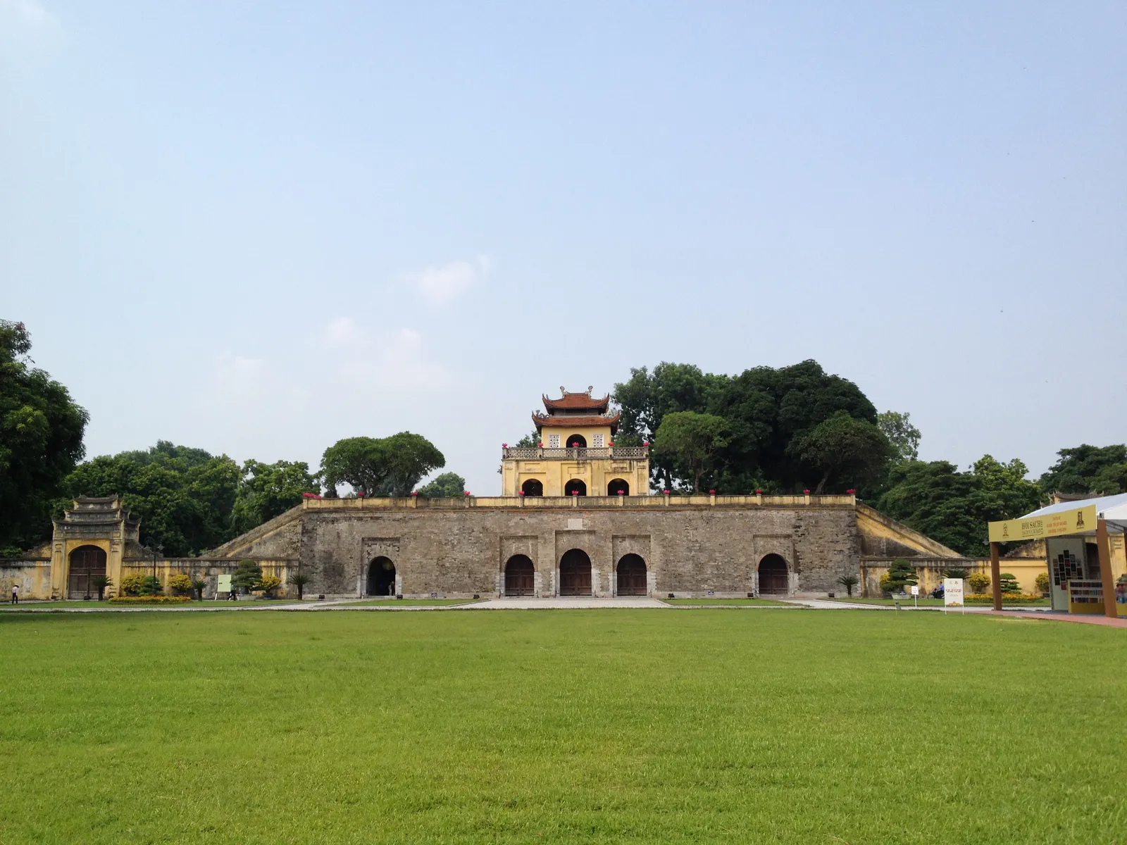 Doan Mon, the yellow stone southern gate of the Imperial Citadel of Thang Long in Hanoi, with three arched openings at ground level and a tiled pavilion on top, seen across a wide lawn
