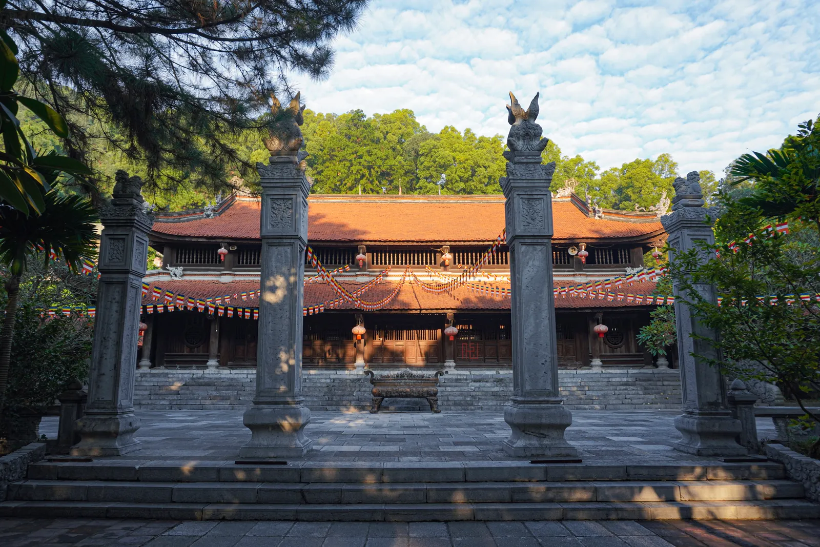 Non Nuoc Pagoda on Ve Linh mountain in Soc Son, a broad red-roofed timber hall seen between two stone pillars topped with carved birds, with forested slopes rising behind it