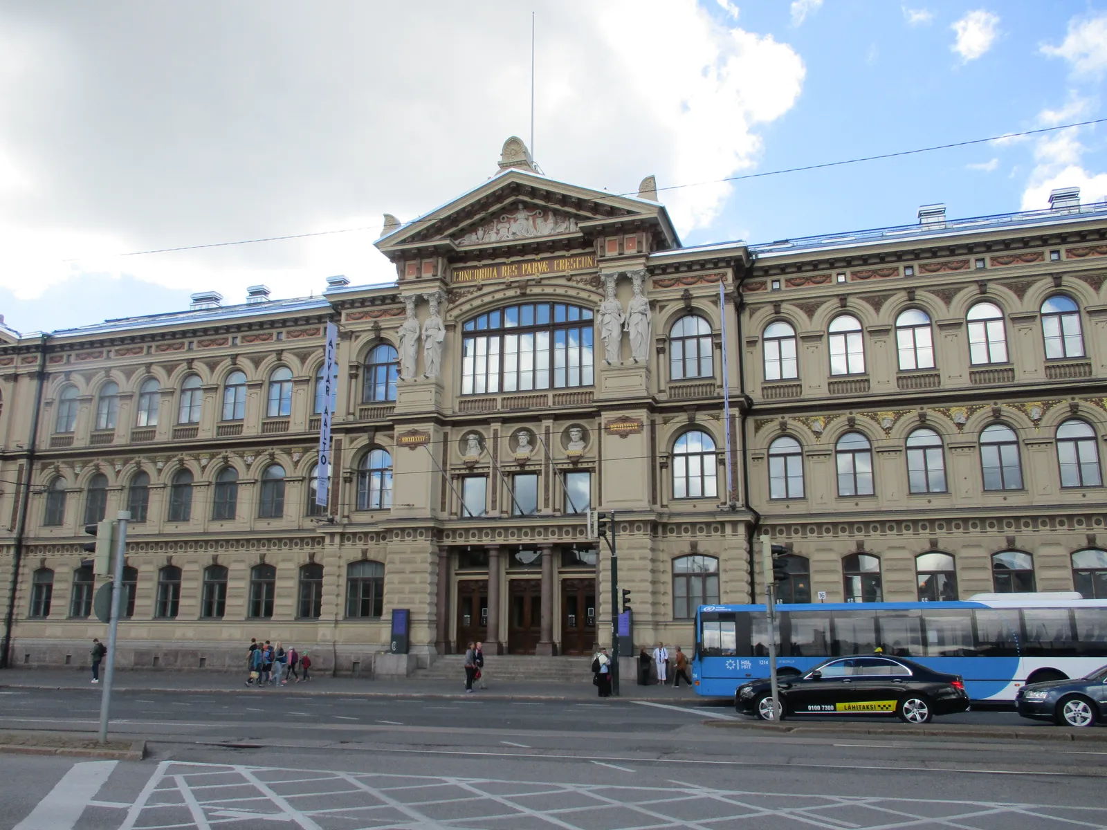 The front of the Ateneum art museum in Helsinki, a long pale 19th-century palace with a pedimented centre, arched ground-floor windows and carved figures set between the upper windows, seen from across the tram tracks
