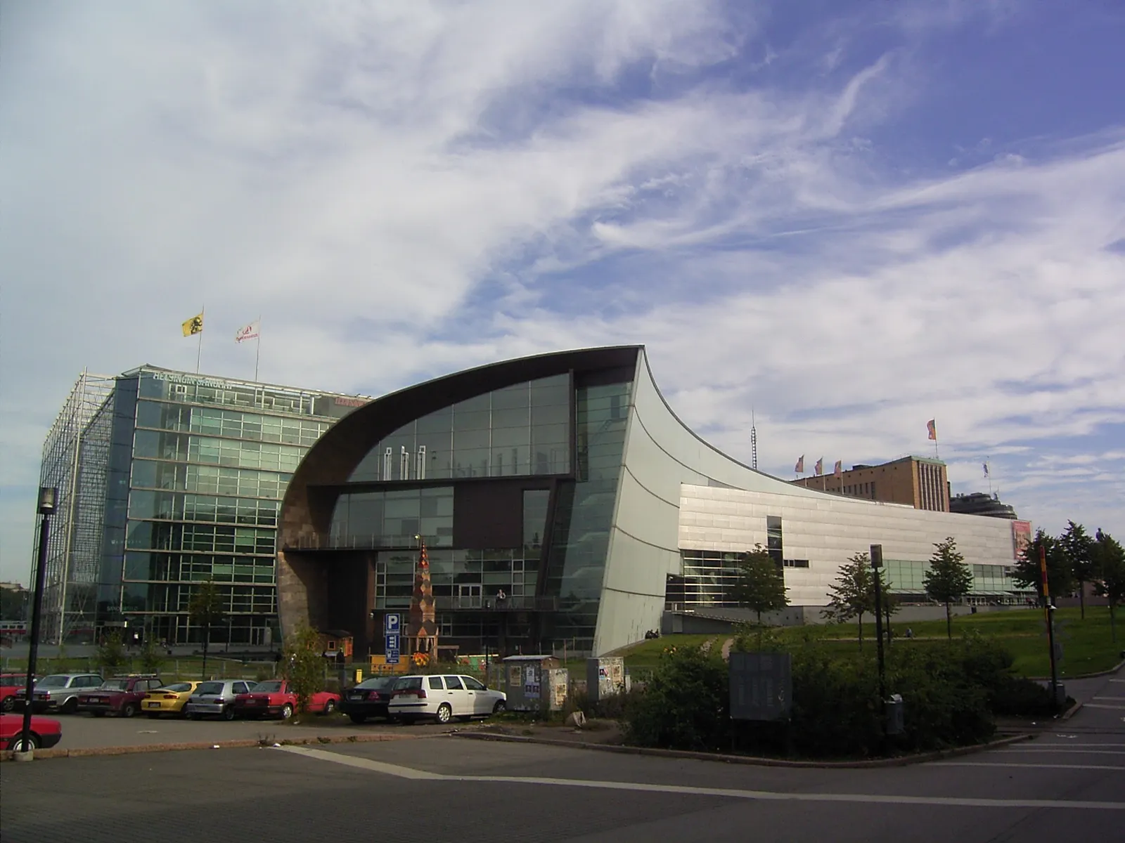 The Kiasma museum in Helsinki, a low building whose dark curved metal flank sweeps round into a long white wall with a band of glazing, with a glass office block and an open square beside it