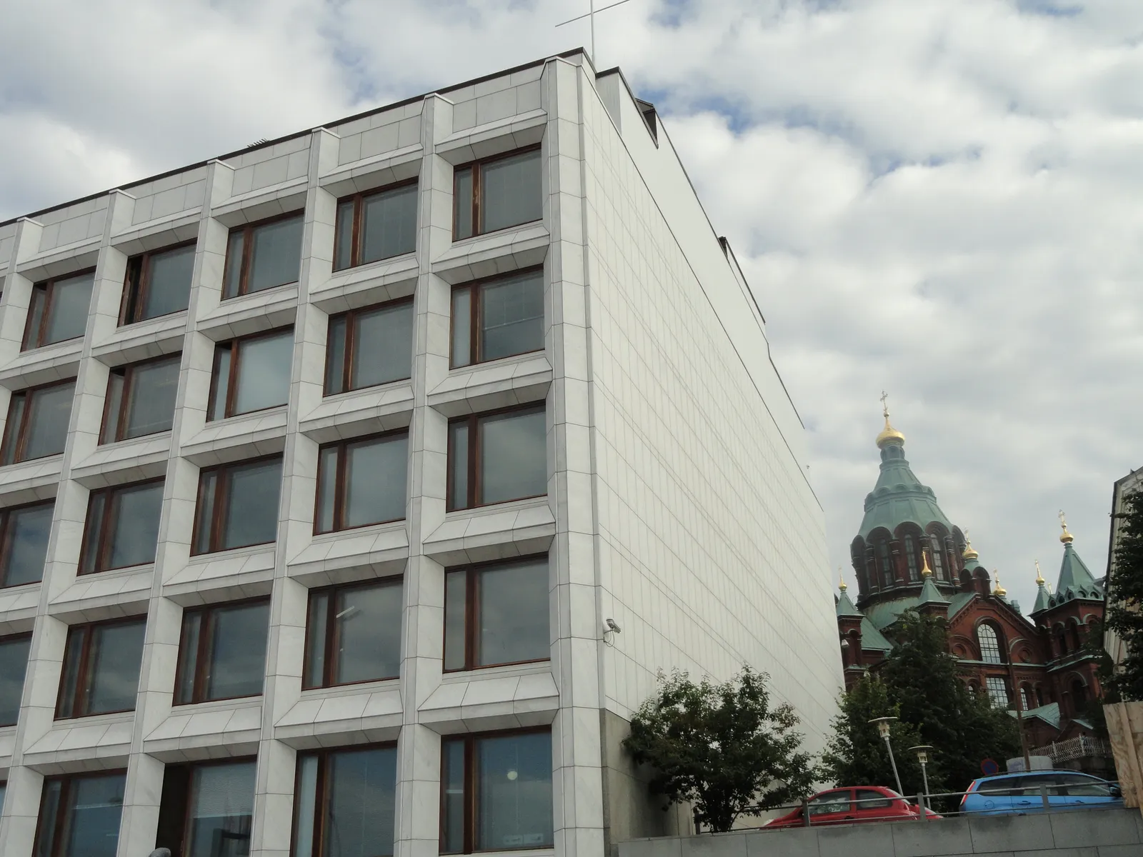 Alvar Aalto's office block at the western end of Katajanokka in Helsinki, a low rectangular building faced entirely in white marble panels with a grid of square windows, with the green domes of Uspenski Cathedral rising behind it