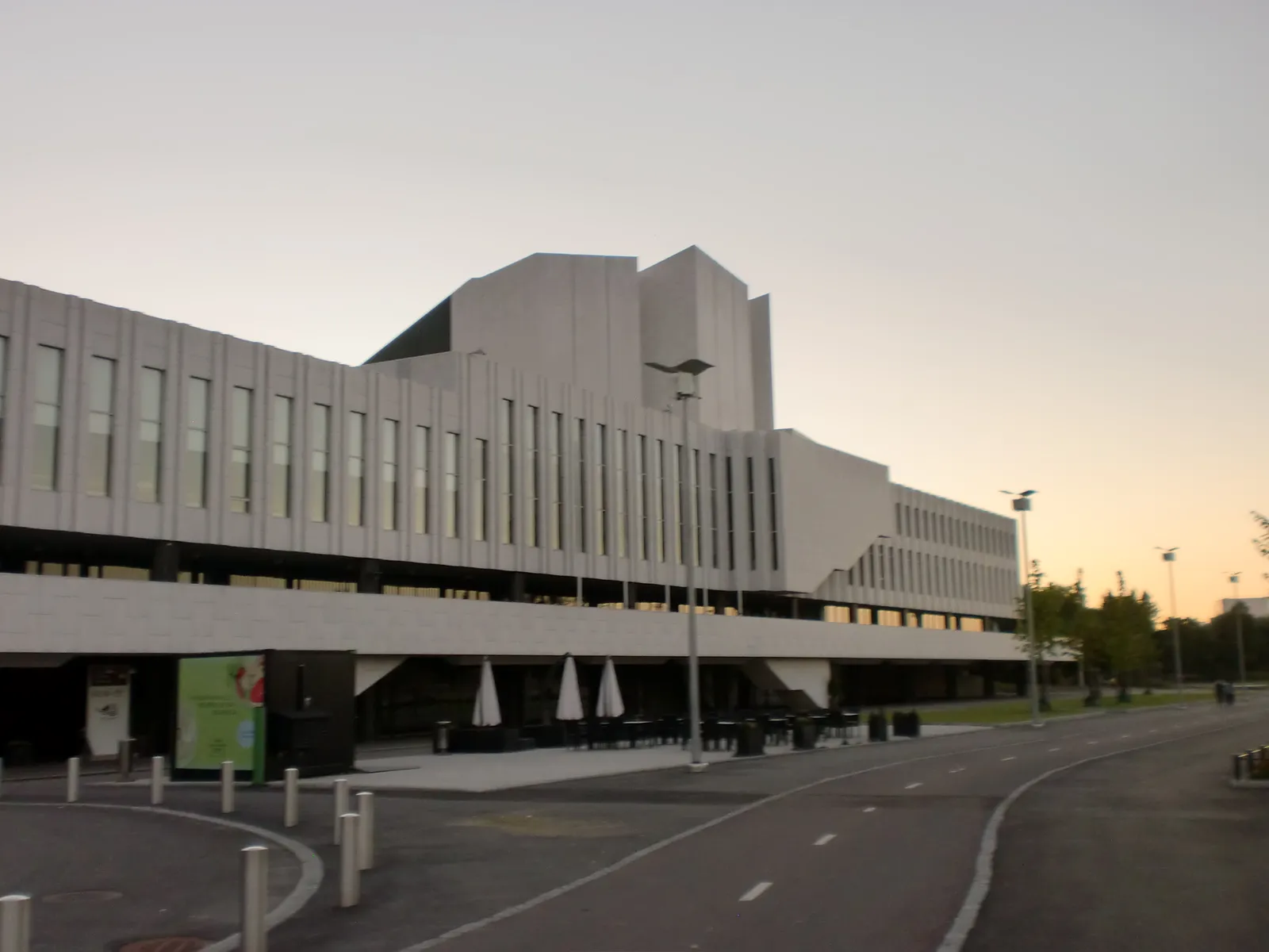 Finlandia Hall in Helsinki at dusk, a long low building faced in white marble panels with vertical ribs, a taller angular block rising over the middle of it, and an empty forecourt with café tables under the overhang