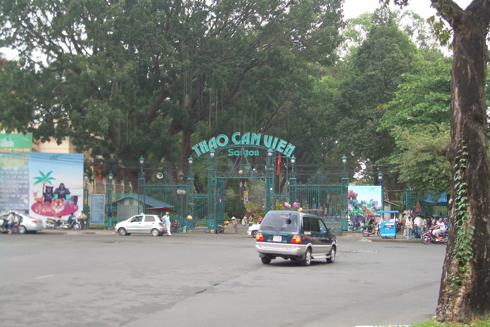 The green wrought-iron gates of the Saigon Zoo and Botanical Gardens with Thao Cam Vien Saigon lettered across the arch above, under the canopy of the old trees inside