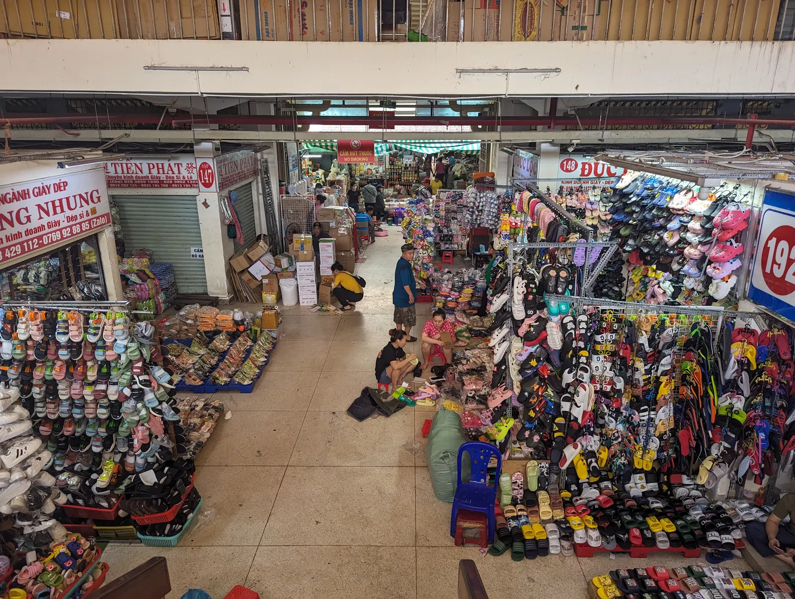 An aisle inside Binh Tay Market seen from the upper gallery, stalls stacked floor to ceiling with shoes and sandals on both sides and a narrow walkway between them