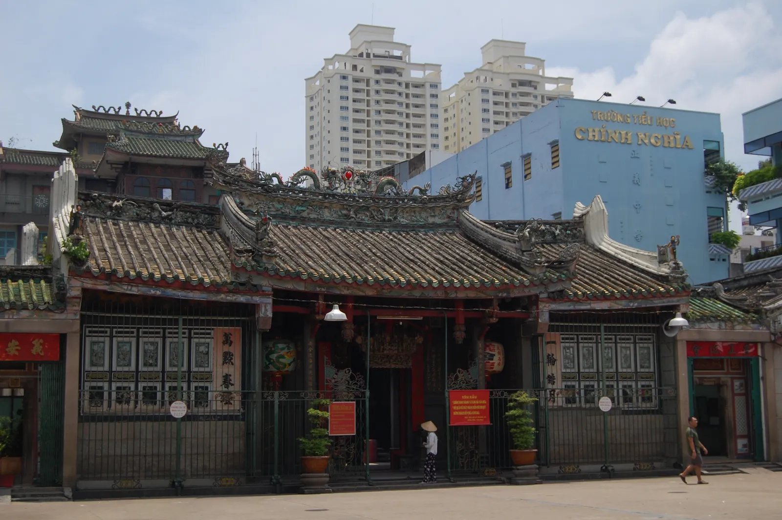 The street frontage of Nghia An Assembly Hall on Nguyen Trai, a low green-tiled roof crowded with ceramic figures above dark carved timber screens and red-panelled doors