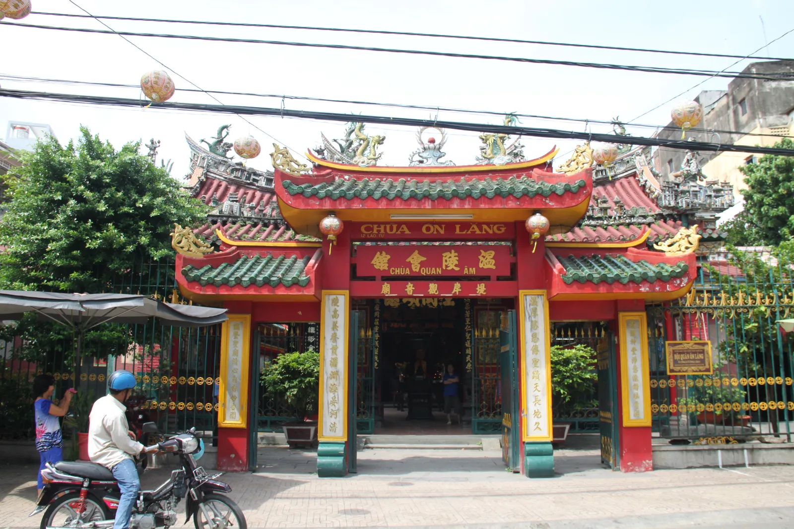 The red and gold entrance gate of On Lang assembly hall in Cho Lon, green glazed roof tiles topped with ceramic dragons and gold Chinese lettering across the lintel