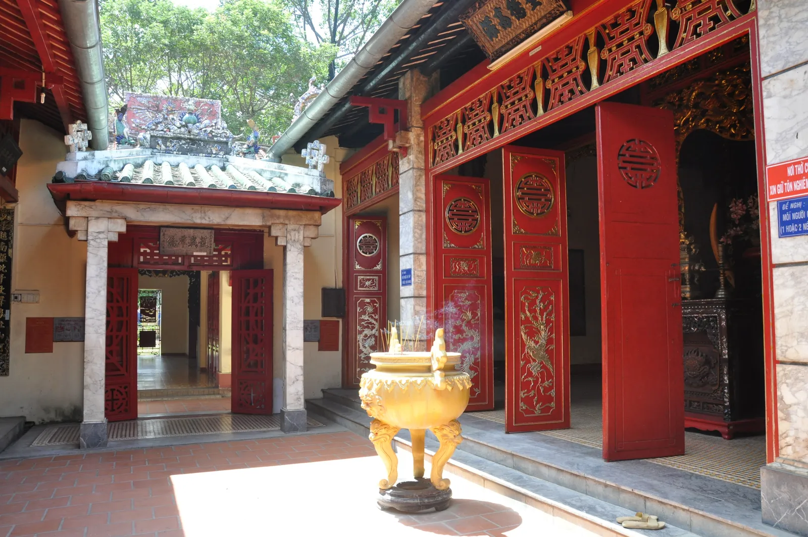 The temple courtyard inside Le Van Duyet's tomb complex, tall red lacquered doors carved with gold panels along a stone-floored veranda, with a bronze incense urn standing in front