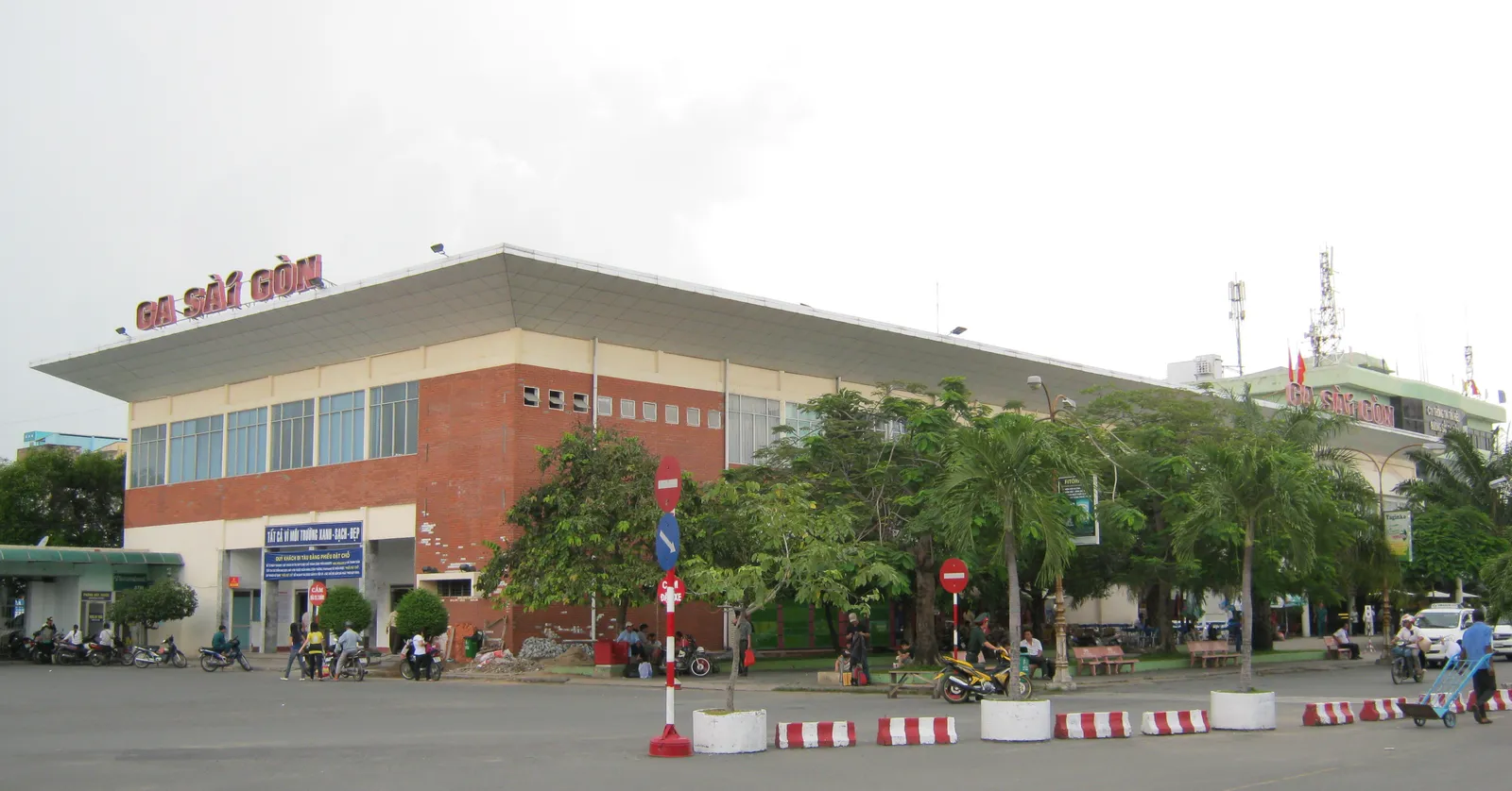 The low brick and concrete frontage of Saigon railway station with GA SAI GON lettered along the upper wall, motorbikes parked at the kerb and palms in the forecourt