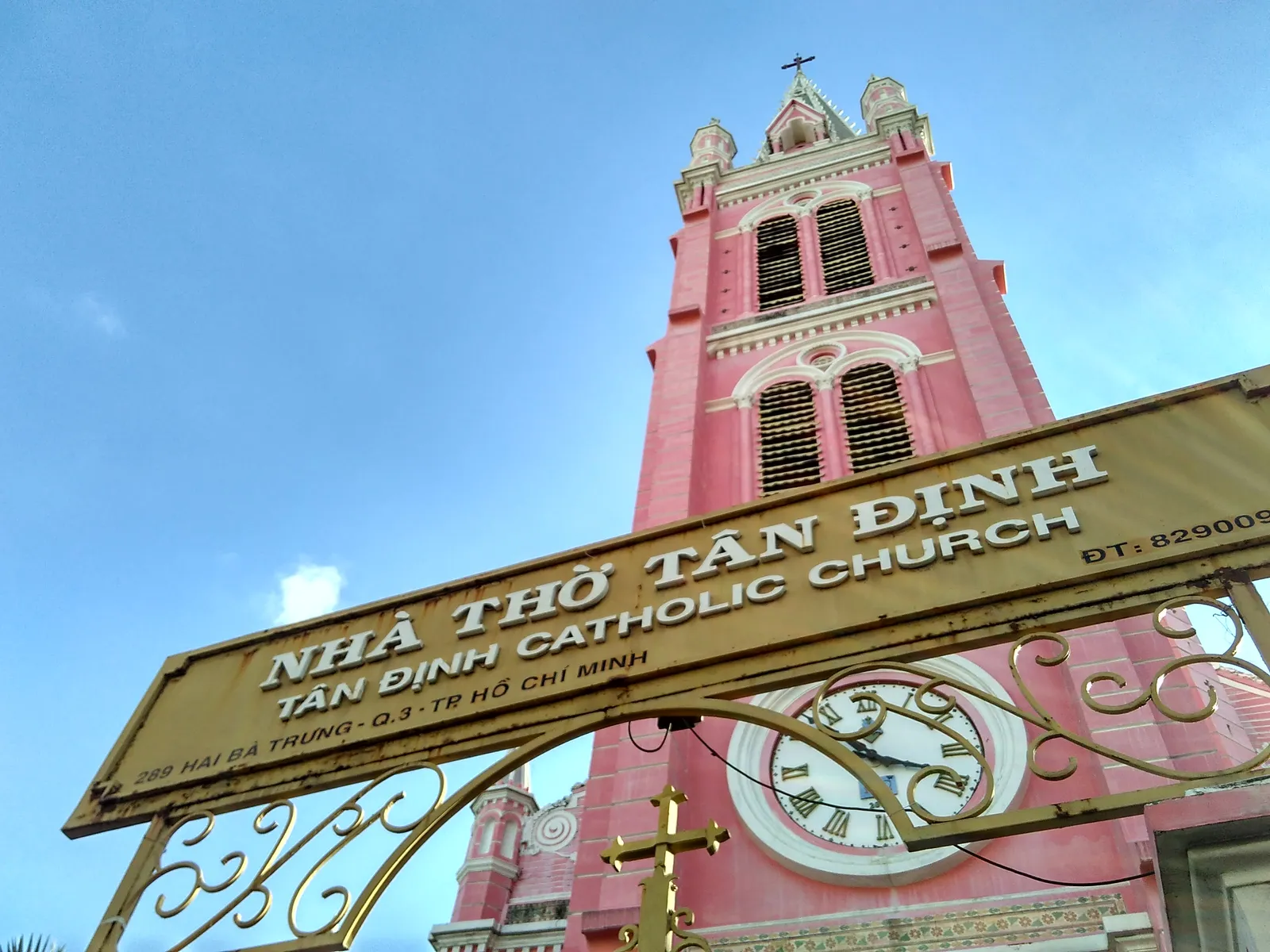 The salmon-pink bell tower of Tan Dinh Church in Ho Chi Minh City rising behind its gold-lettered gateway sign reading Nha Tho Tan Dinh, Tan Dinh Catholic Church