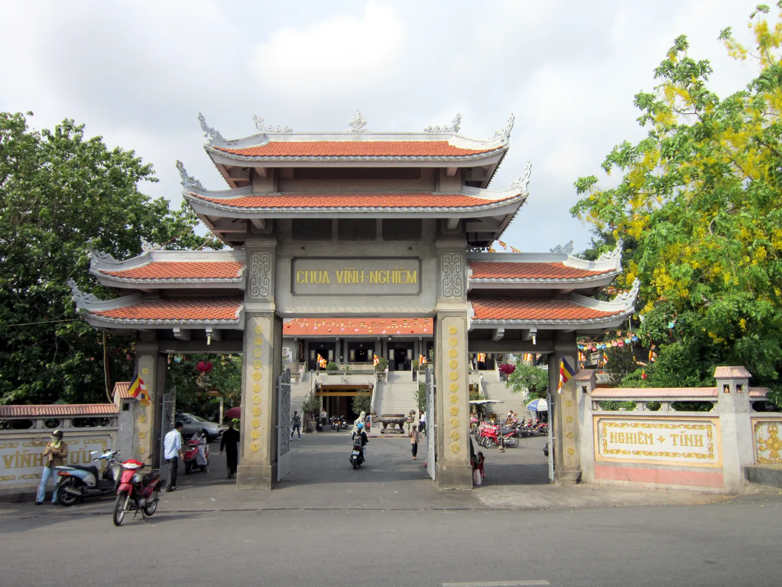 The three-arched tiled gateway of Vinh Nghiem Pagoda on Nam Ky Khoi Nghia in Ho Chi Minh City, its name in gold across the centre span with motorbikes passing underneath