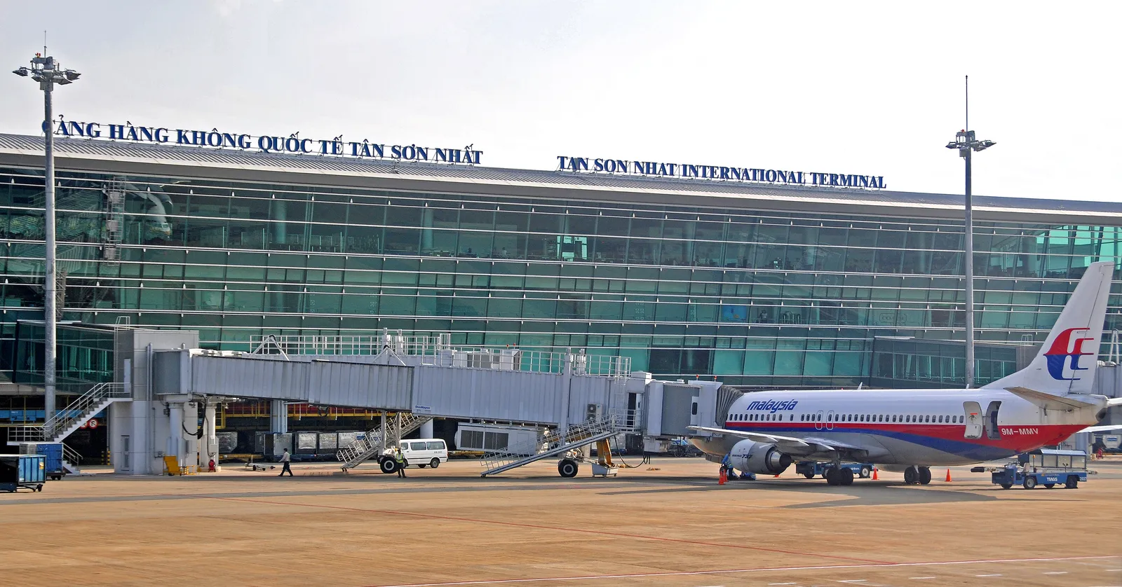 The airside frontage of Tan Son Nhat International Airport's international terminal, its name in Vietnamese and English along the roofline above the glass, with a jet bridge and an aircraft parked at the stand