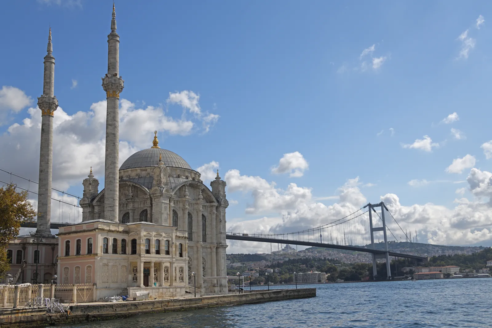 Ortaköy Mosque on the edge of the Bosphorus in Istanbul, a small ornate mosque with two slender minarets standing at the water's edge, with the suspension bridge crossing the strait behind it