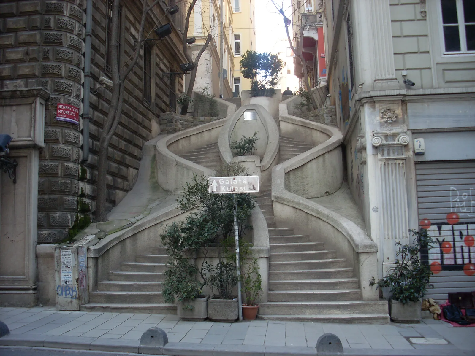 The Camondo Stairs in Istanbul, a pale stone staircase splitting into two curving flights that loop around each other between tall 19th-century buildings on a steep narrow street