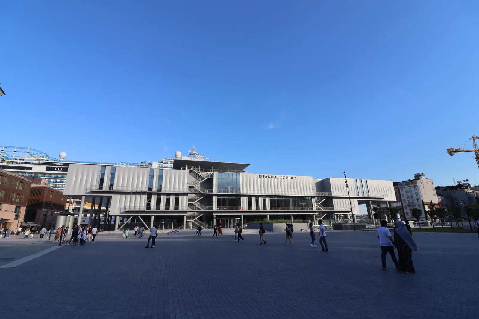 The long, low Istanbul Modern museum building on the Galataport waterfront, clad in pale metal panels with a glass section in the middle, across a wide paved square