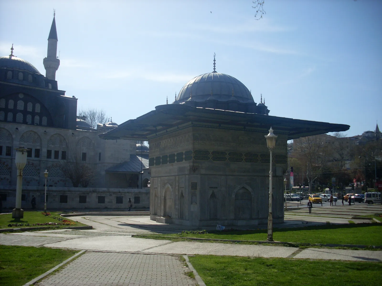 The square, domed stone Tophane Fountain with its wide overhanging roof in Istanbul, with the dome and minaret of the Kılıç Ali Paşa Mosque behind it