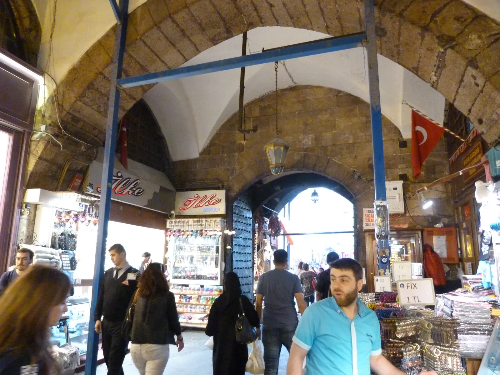 Inside Istanbul's Spice Bazaar, a stone-vaulted arcade lined with shopfronts selling sweets and spices, Turkish flags hanging from the ceiling and shoppers moving down the middle of the aisle