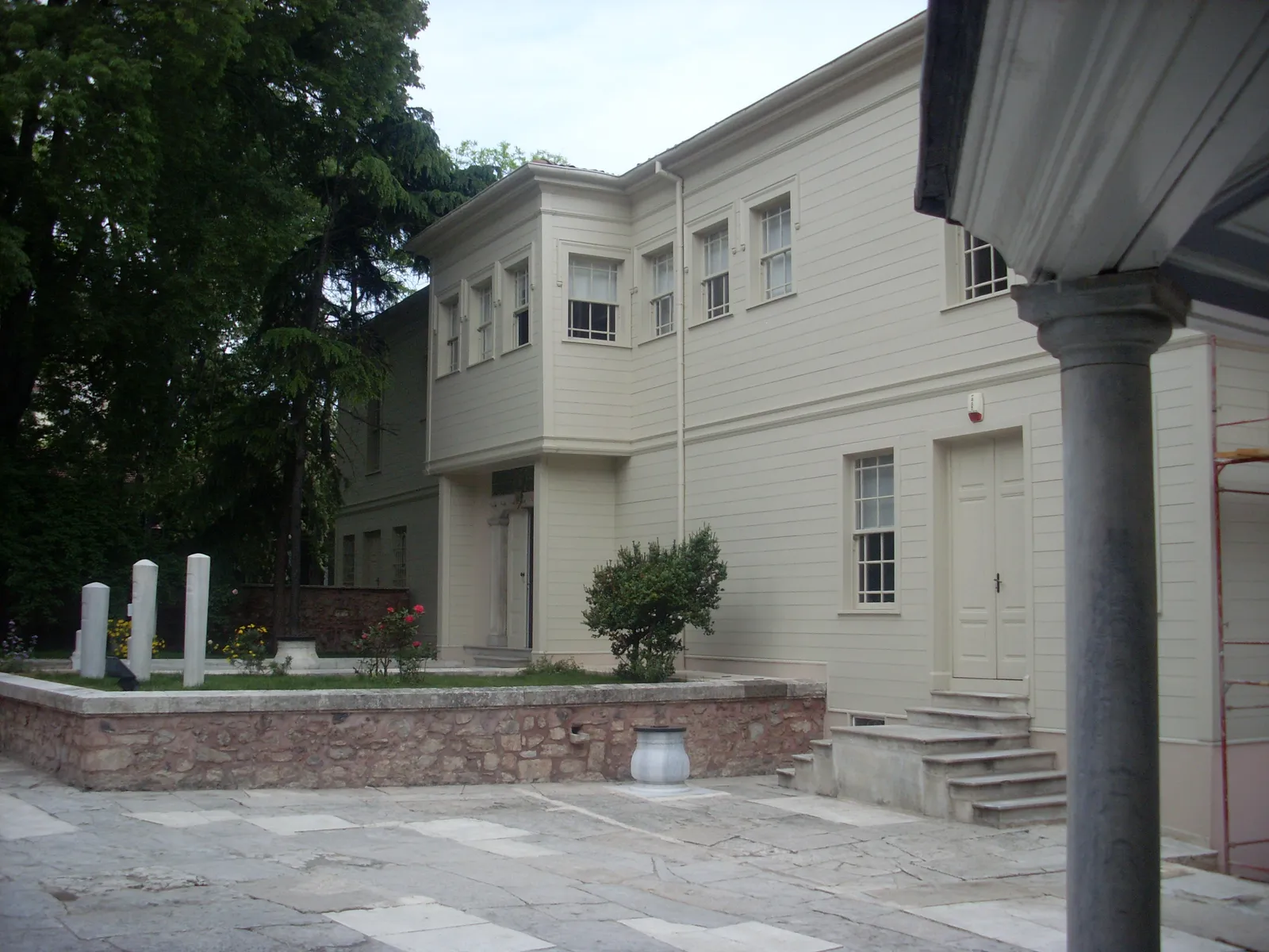 The pale timber semahane building of the Galata Mevlevi House Museum in Istanbul, two storeys with rows of shuttered windows, standing in a paved courtyard behind a low stone wall