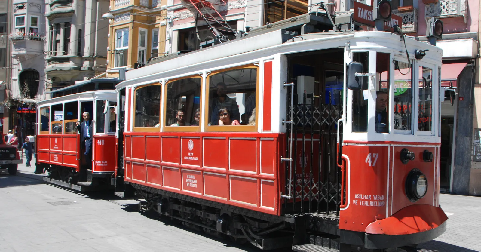 The red single-deck nostalgic tram on İstiklal Avenue in Istanbul, number 47 on its front, running between crowds and 19th-century shopfronts on the pedestrian street