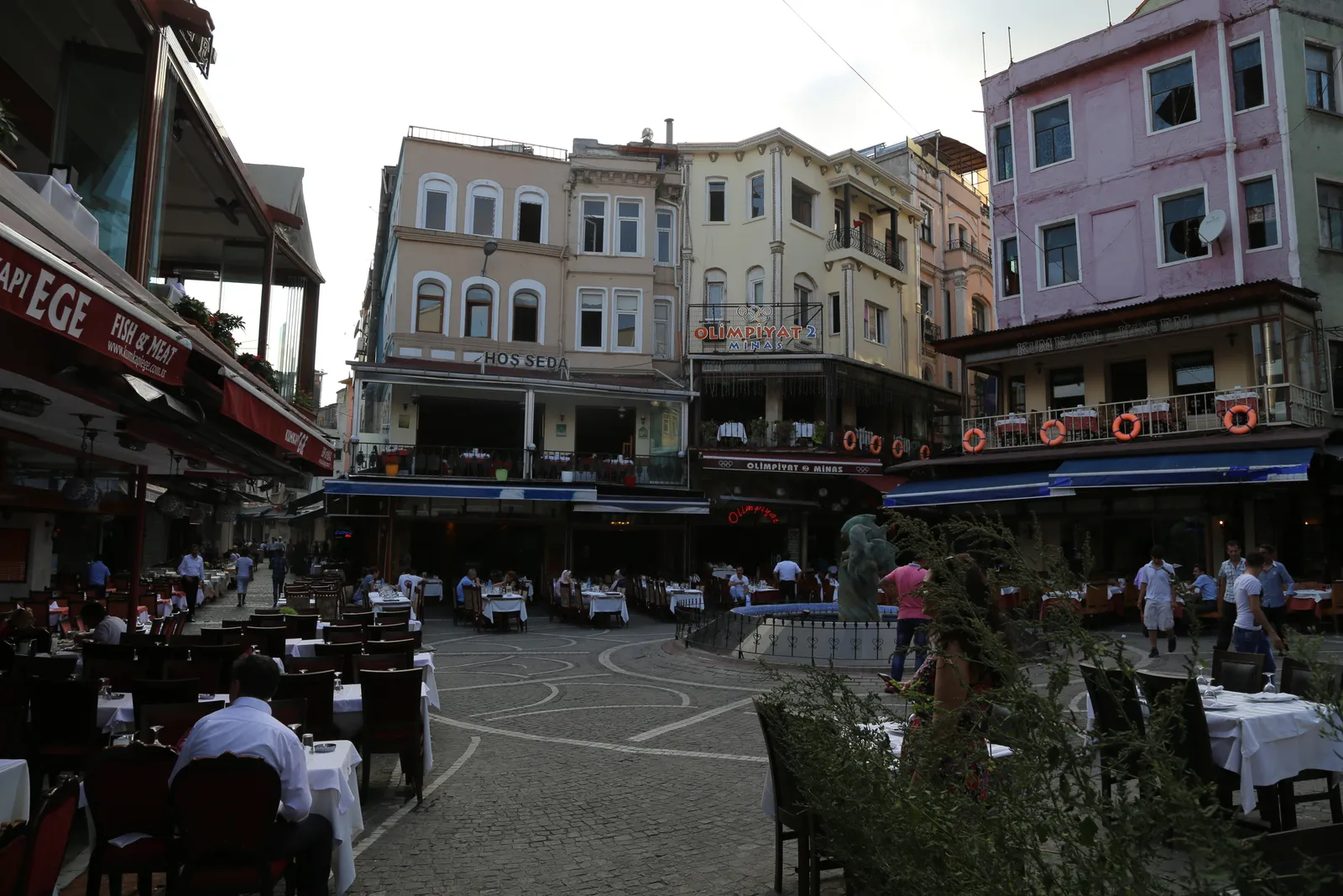 The restaurant square at Kumkapı in Istanbul, tables laid with white cloths filling the cobbles between pastel four-storey houses with awnings and terraces above them