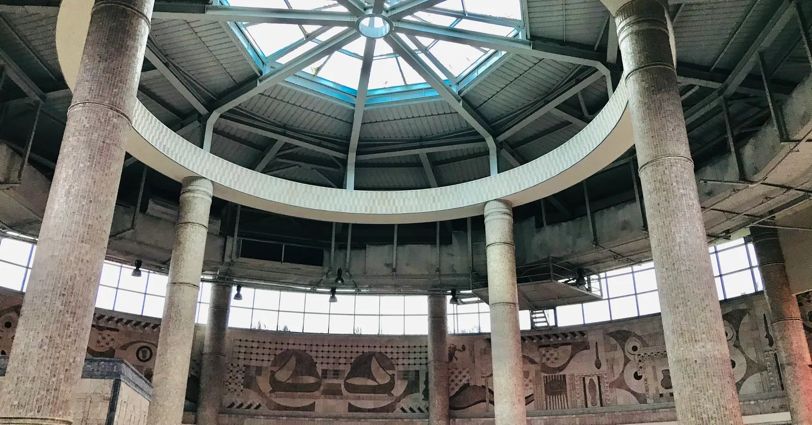 The central hall of Yenikapı station in Istanbul, a circular concourse ringed by heavy stone columns under a glazed dome, with carved relief panels along the wall above the ticket gates