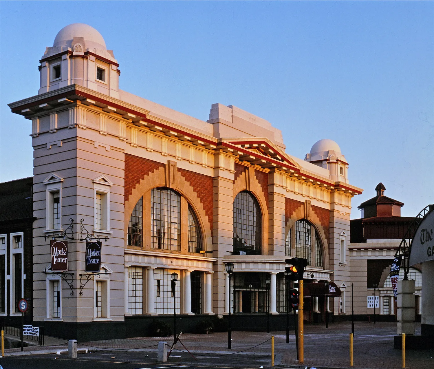 The Market Theatre in Newtown, Johannesburg, in low evening light, a cream and red-brick market building with three tall arched windows, a pedimented centre and small domed turrets at either end