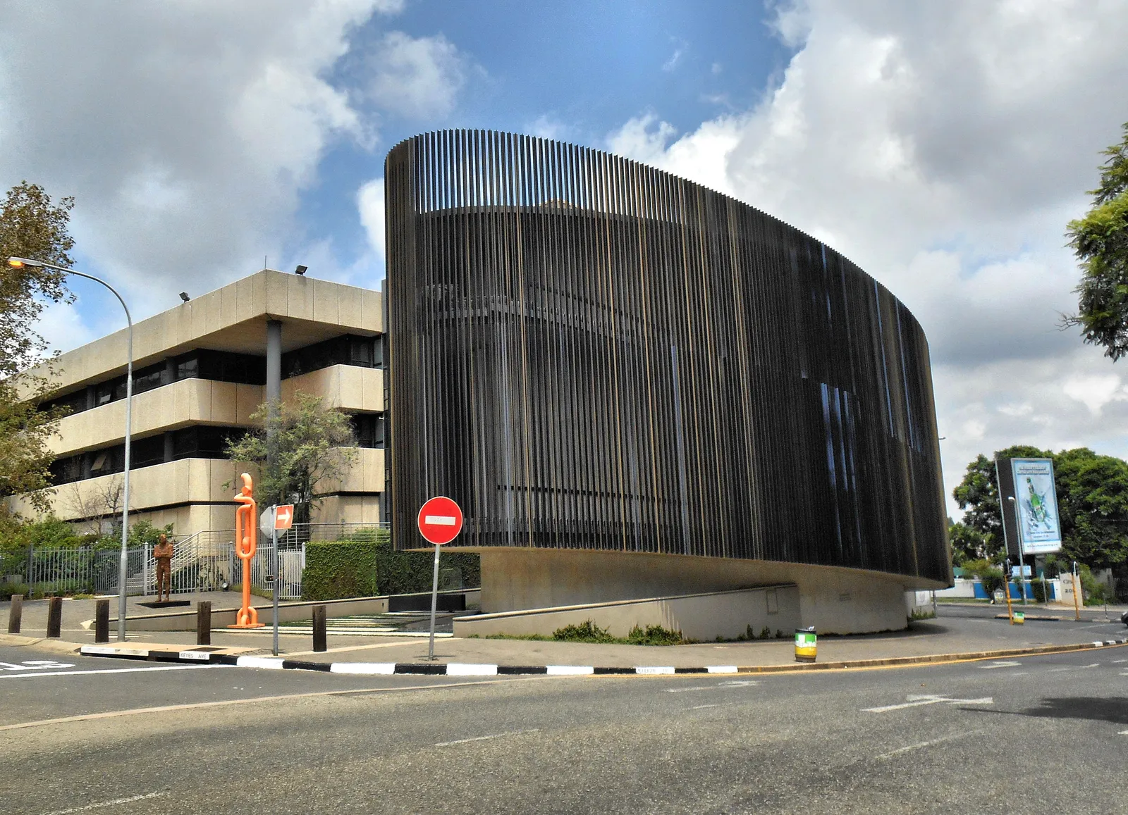 Circa on Jellicoe in Rosebank, Johannesburg, an oval gallery building on a street corner clad in tall dark vertical slats above a low concrete base, with a no-entry sign and street lamps in front of it