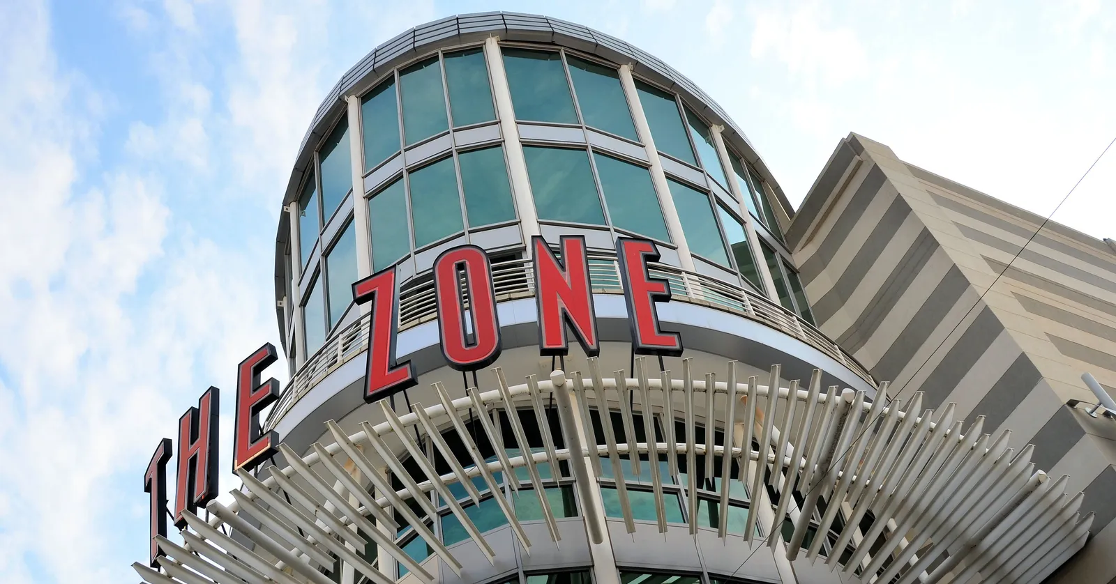 The Zone shopping centre in Rosebank, Johannesburg, a glass drum on the corner of the building with THE ZONE in large red letters across it, under a spreading white steel canopy