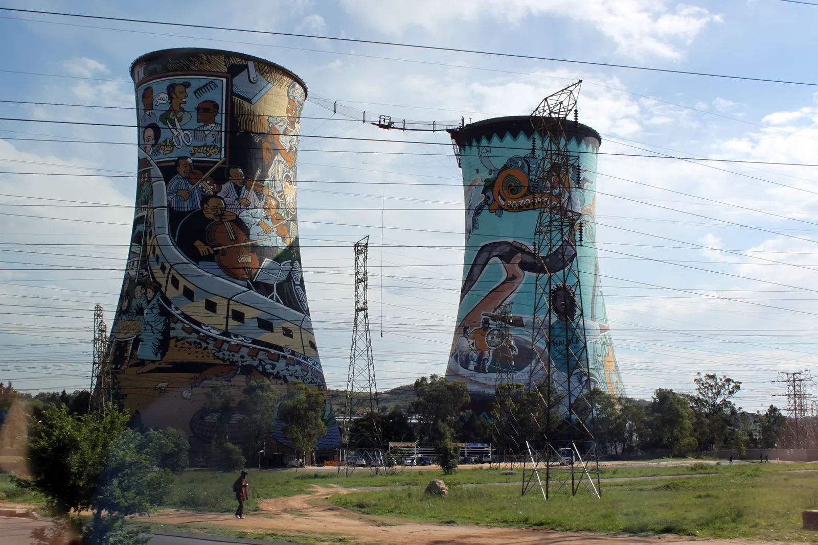 The two cooling towers of the old Orlando power station in Soweto, painted from base to rim with murals of township scenes, with the cables of a suspension bridge strung between their tops