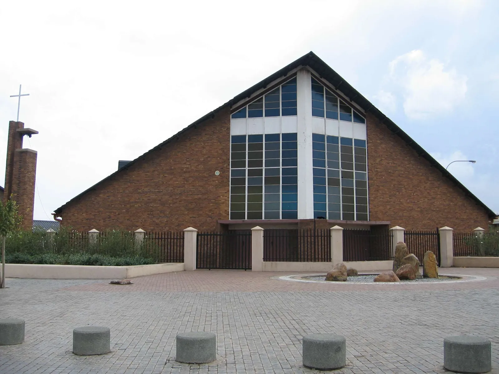 Regina Mundi church in Rockville, Soweto, a wide brick building with a steep gable front, a tall grid of windows above the doors and a freestanding brick tower carrying a cross beside it
