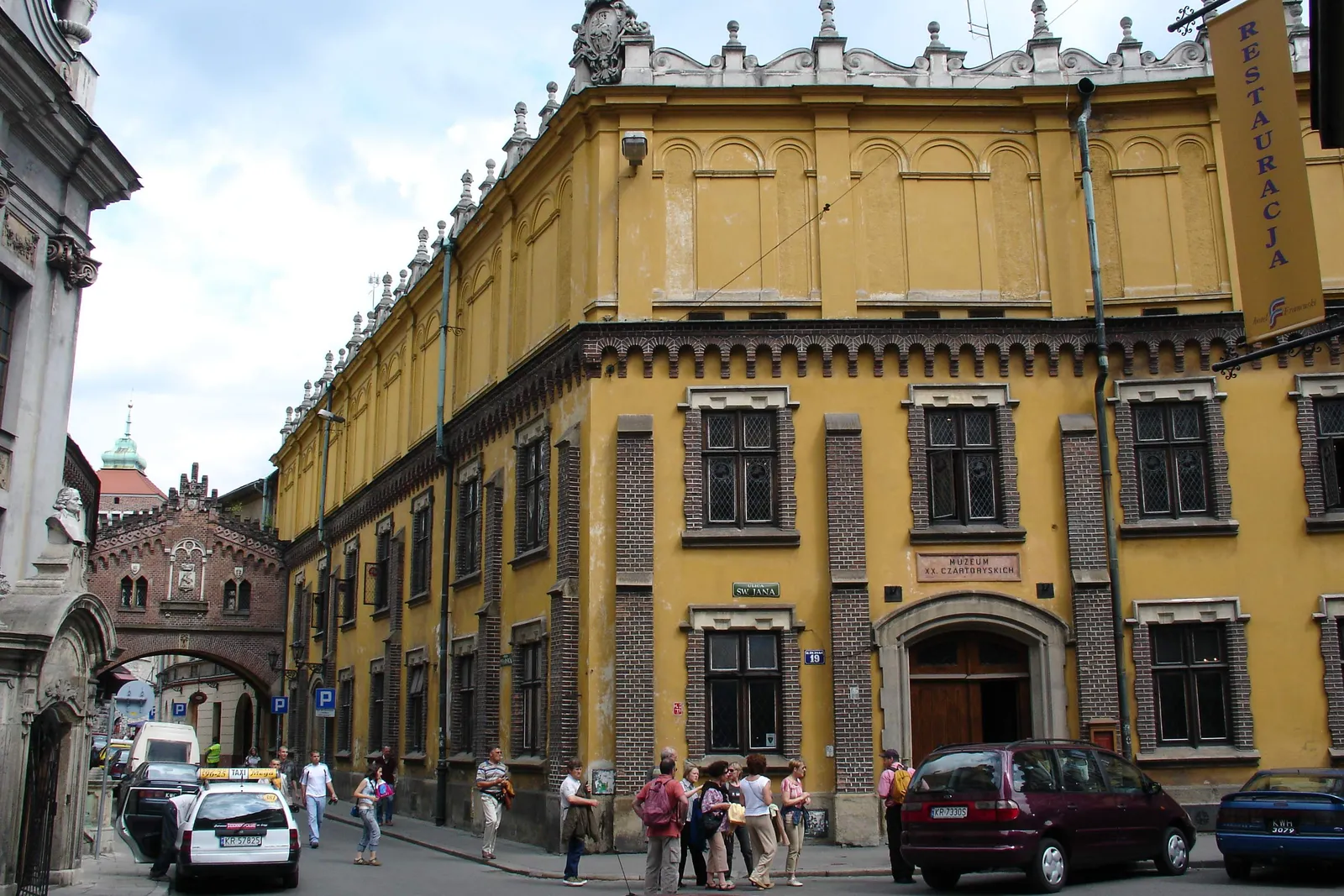 The yellow corner building of the Czartoryski Museum on ulica Pijarska in Kraków, with an arcaded bridge crossing the street between two of its wings further down the block